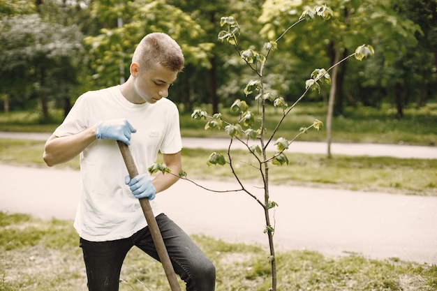 Vrijwilliger plant een boom. Europese jongen in handschoenen die spade gebruiken. Park instelling.