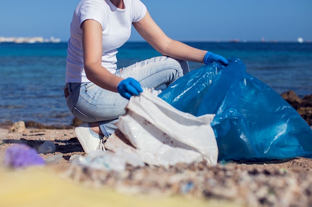 Vrijwilliger van de vrouw met grote blauwe zak die vuilnis op strand verzamelt. Milieuvervuiling concept