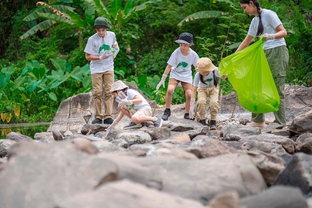 Foto vrijwilligers uit azië en kinderen verzamelen plastic flessen die door de stroom in vuilniszakken stromen