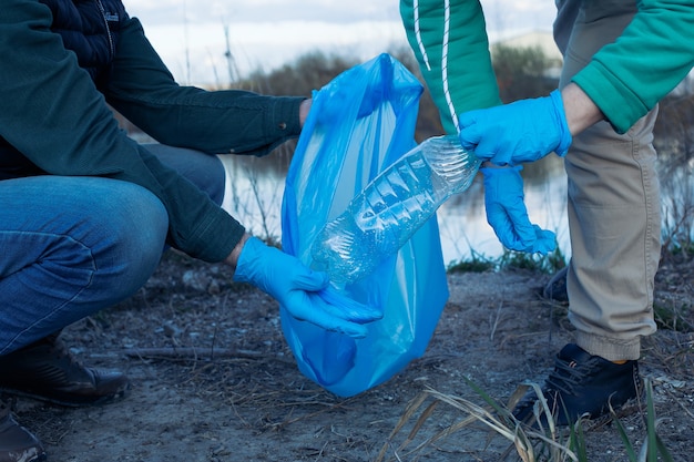 Vrijwilligers verzamelen plastic flessen in zakken, close-up van handen, het concept van ecologie en bescherming van de aarde.