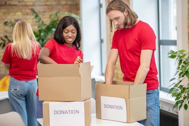 Vrijwilligersprogramma. Jonge gefocuste blanke man en donkerhuidig meisje in identieke t-shirts die donaties in dozen verpakken