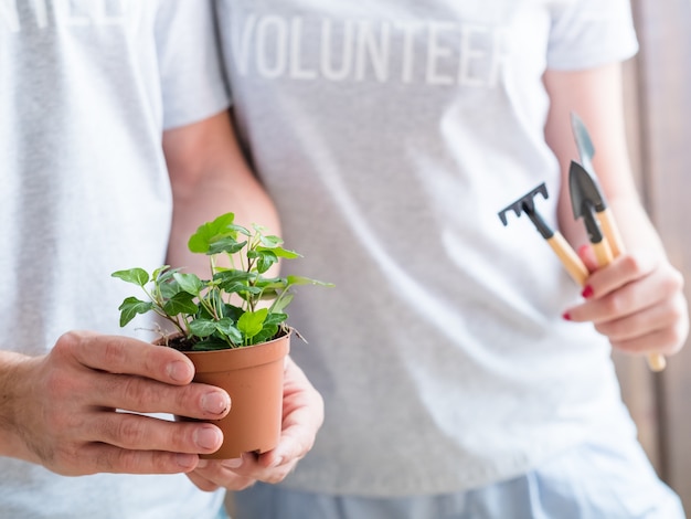 Vrijwilligerswerk levensstijl. Denk groen concept. Echtpaar met kamerplant en tuingereedschap.
