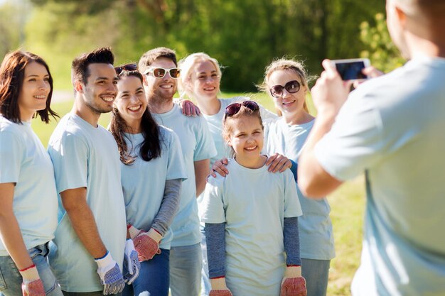 vrijwilligerswerk, liefdadigheid, mensen, teamwerk en milieuconcept - groep gelukkige vrijwilligers die foto's maken met een smartphone in het park