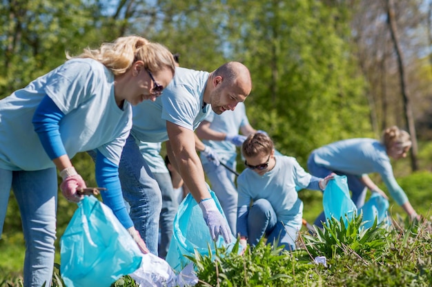 vrijwilligerswerk, liefdadigheid, schoonmaak, mensen en ecologisch concept - groep gelukkige vrijwilligers met vuilniszakken schoonmaakgebied in park