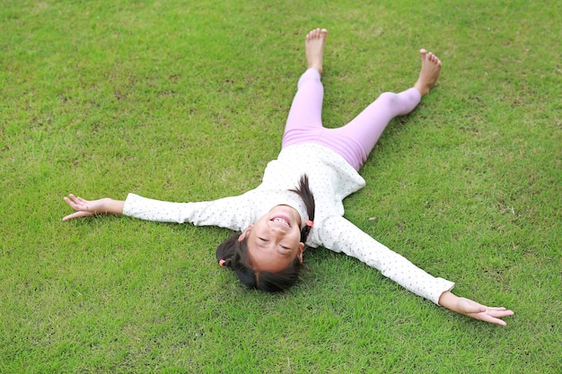 Vrolijk Aziatisch meisje dat op groen gazon ligt Gelukkig kind ligt op gras en kijkt naar de camera