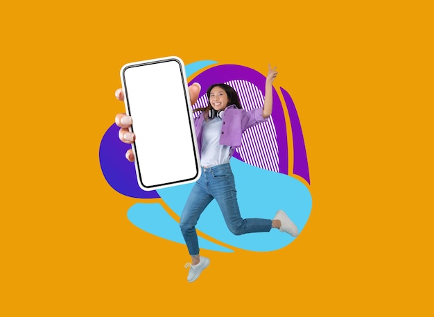 Vrolijk Aziatisch tienermeisje die met lege smartphone over kleurrijke abstracte achtergrond springen