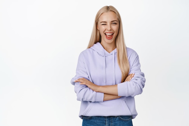 Vrolijk blond meisje dat naar de camera knipoogt en naar je glimlacht met vertrouwen op een witte achtergrond