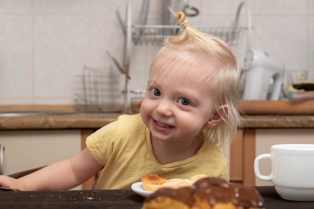 Vrolijk blond meisje in de keuken eet koekjes Gelukkig kind