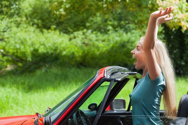 Vrolijk blonde die van haar rode cabriolet genieten