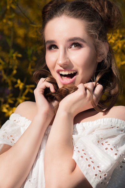 Vrolijk brunette meisje met mooie make-up poseren in de buurt van de bloeiende gele bloemen