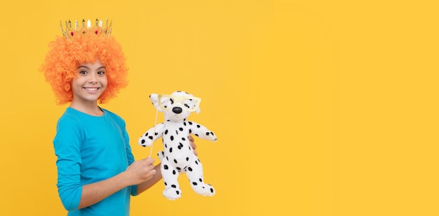 Vrolijk egoïstisch kindmeisje met krullende pruik en prinsesdiadeem houdt speelgoedhond vast, kopieer ruimte speelgoedwinkel