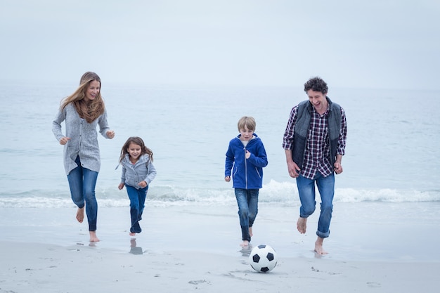 Vrolijk familie speelvoetbal op zee kust tegen hemel