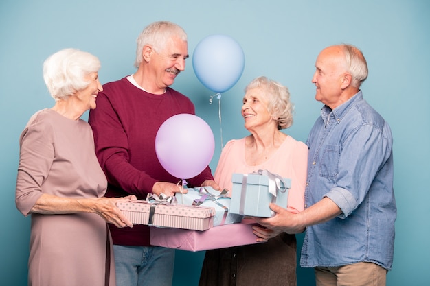 Vrolijk gezelschap van vriendelijke gepensioneerden met ballonnen en geschenkverpakkingen die vakantie of jubileum vieren