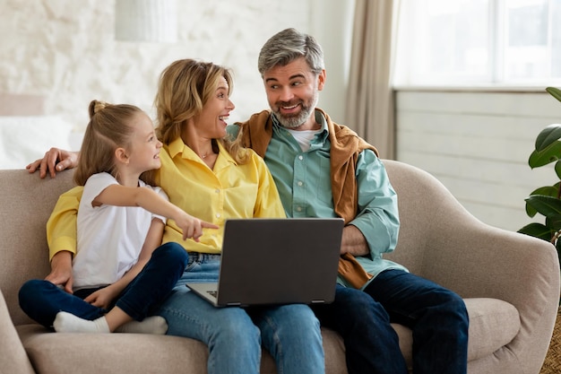Vrolijk gezin van drie met behulp van laptopcomputer binnenshuis surfen op internet