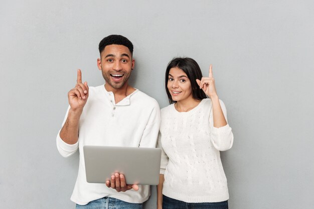 Vrolijk houdend van paar dat zich over grijze muur bevindt en laptop met behulp van