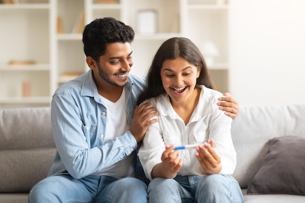 Vrolijk Indisch echtpaar met positieve zwangerschapstest op de bank