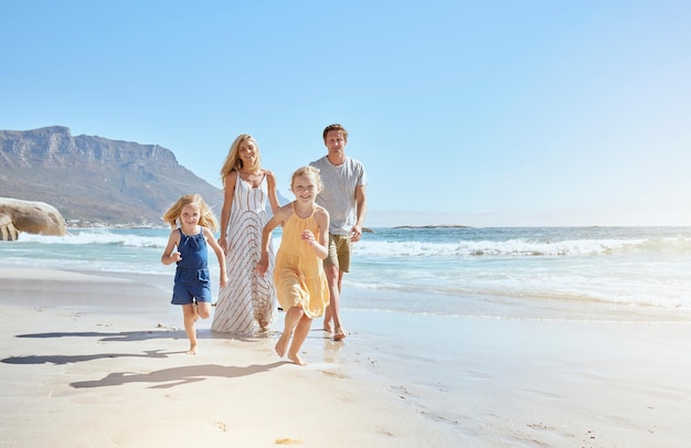 Vrolijk jong gezin met twee kinderen die op het strand rennen en genieten van de zomervakantie Twee energieke kleine meisjes die vooruit rennen terwijl hun moeder en vader op de achtergrond volgen
