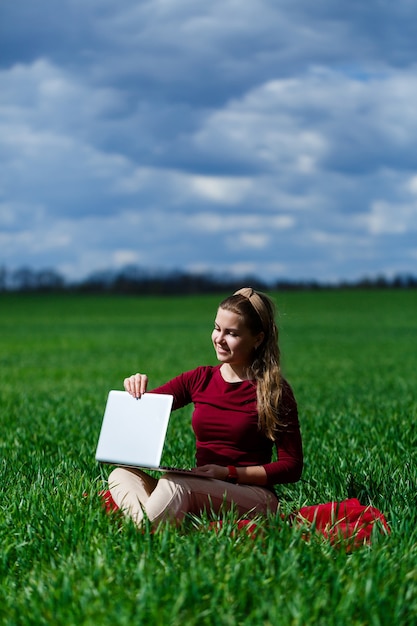 Vrolijk jong meisje op het gras met een laptop op haar schoot. Hij hief zijn handen omhoog en lachte. Geluk in de levensstijl van een klassieke student. Werk aan de natuur. Rust na een goede werkdag.