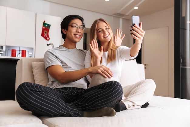 Vrolijk jong stel, dat een selfie neemt terwijl ze thuis op een bank zitten