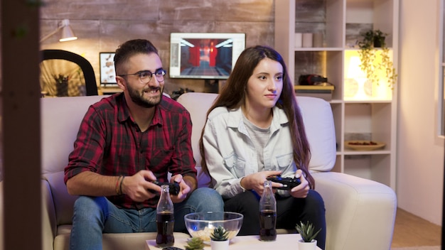 Vrolijk jong stel dat op het paar zit en videogames speelt op televisie met behulp van controllers.