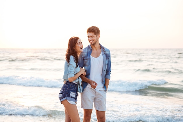 Vrolijk jong stel lachen en wandelen op het strand