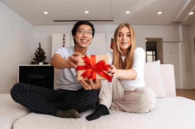 Vrolijk jong stel, zittend op een bank thuis, met huidige doos