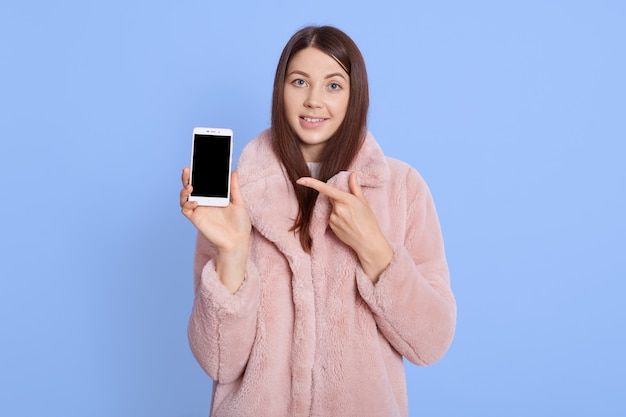 Vrolijk jong vrouwenmeisje in roze bontjas stellen geïsoleerd over blauw