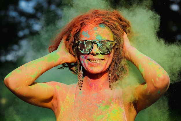 Vrolijk Kaukasisch model met een zonnebril, poserend in een wolk van groene Holi-verf