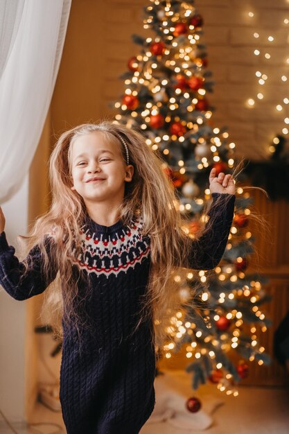 Vrolijk kerstconcept. Het kind danst vrolijk bij de kerstboom thuis. Vrolijk kerstfeest thuis.