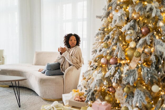 Foto vrolijk kerstfeest afrikaans-amerikaanse vrouw met een kopje warme drank koffie thee zit bij de kerstboom