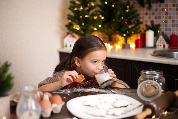 Vrolijk kerstfeest Een grappig lief meisje in een gezellig ingerichte keuken bakte kerstkoekjes en eet ze op Lifestyle Warme tinten