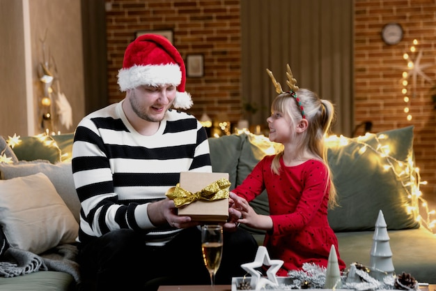 Vrolijk kerstfeest en een gelukkig nieuwjaar. Cadeau verrassing. Een klein blij lachend dochtermeisje opent met verbazing een kerstcadeau. Vader geeft zijn dochter cadeau binnenshuis in feestelijk versierd huis