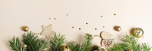 Vrolijk kerstfeest en een gelukkig nieuwjaar. Vuren takken met kerstelementen op een beige achtergrond. Gouden elementen. lang formaat