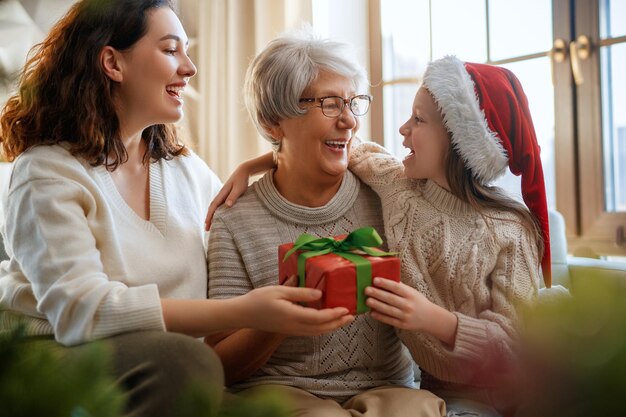 Foto vrolijk kerstfeest en gelukkige feestdagen vreugdevol kind dat geschenken presenteert aan moeder en grootmoeder ouders