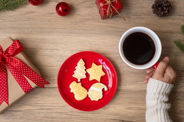 Vrolijk kerstfeest met vrouw hand met koffiekopje en zelfgemaakte cookie op tafel. Kerstavond, feest, vakantie en gelukkig nieuwjaar concept