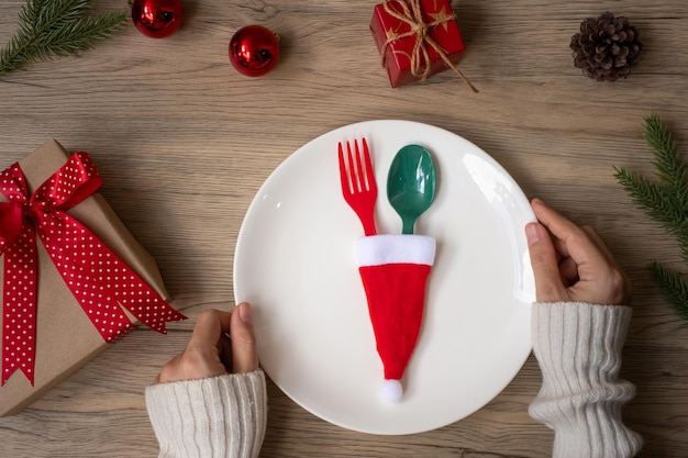 Vrolijk kerstfeest met vrouw hand met plaat, vork en lepel op houten tafel achtergrond. Kerstmis, feest en gelukkig nieuwjaarsconcept