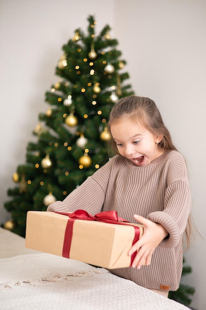 Vrolijk kerstfeest Portret van een schattig meisje met een cadeau in haar handen tegen de achtergrond van een versierde kerstboom Lifestyle