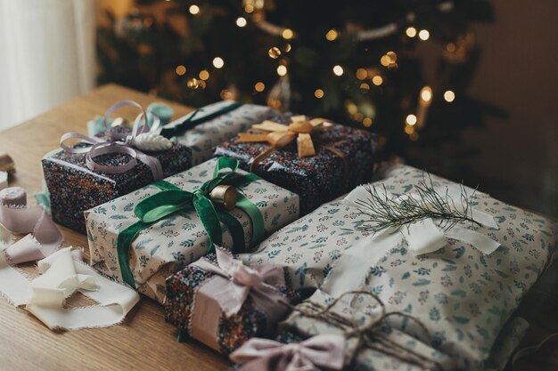 Vrolijk kerstfeest Stijlvol kerstcadeau feestelijk inpakpapier linten vintage ornamenten koperen klokken op houten tafel op de achtergrond van sfeervolle kerstboomverlichting