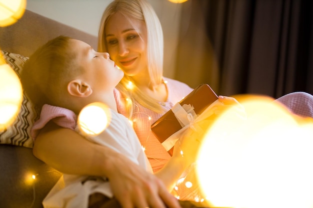 Vrolijk kerstgezin moeder en kinderen met magisch cadeau thuis quarantaine zelfisolatie covid virus slinger gloed