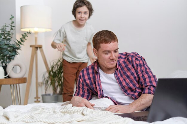 Vrolijk kind dat strijdt om de aandacht van papa terwijl hij probeert te ontspannen met een laptop en series die de essentie van het gezinsleven vastleggen