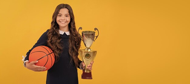 Vrolijk kind houdt basketbalbal en kampioensbeker op geel achtergrondsportsucces Horizontaal