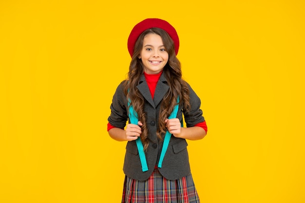 Vrolijk kind in schooluniform met baret en rugzak op gele achtergrond leerling