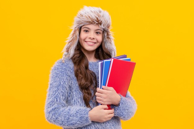 Vrolijk kind in sweater en oorflaphoed met werkboek over geel onderwijs als achtergrond