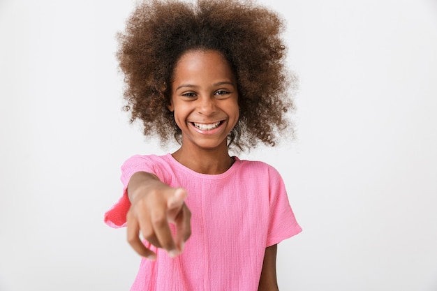 Vrolijk klein Afrikaans meisje met een roze blouse die geïsoleerd over een witte muur staat, met de vinger naar voren