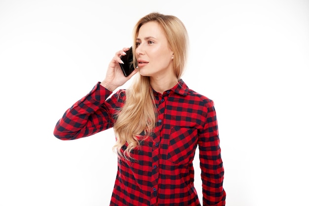 Vrolijk lachend blond meisje in casual pratende smartphone op witte studio achtergrond