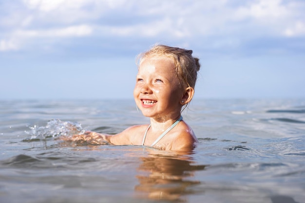 Vrolijk lachend kind blond meisje zwemmen in de zee op een zomerdag.