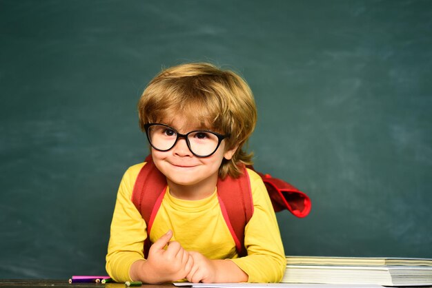 Vrolijk lachend kind op het schoolbord schattige jongen met blije gezichtsuitdrukking in de buurt van bureau met schools...