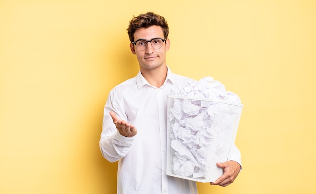 Vrolijk lachend met vriendelijke, zelfverzekerde, positieve blik, aanbieden en tonen van een object of concept. prullenbak papier concept