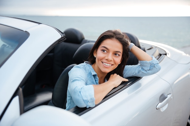 Vrolijk lachende brunette vrouw rusten in haar cabriolet geparkeerd op het strand