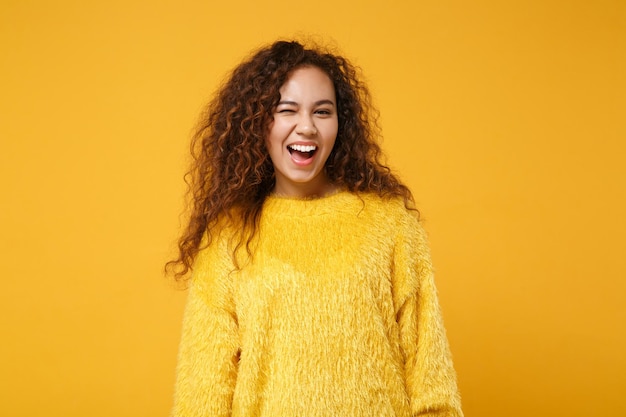 Vrolijk lachende jonge afro-amerikaanse meisje in bont trui poseren geïsoleerd op geel oranje muur achtergrond, studio portret. mensen oprechte emoties levensstijl concept. bespotten kopie ruimte. knipperend.